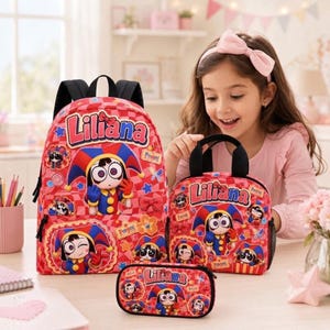 May include: A red and pink checkered backpack, lunch bag, and pencil case set featuring the name Liliana and a cartoon jester character. Each item displays the name Liliana in blue letters with a red outline and various jester illustrations.