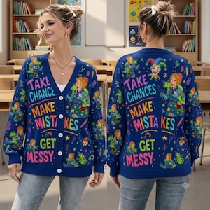 May include: A navy blue V-neck button-down cardigan featuring a colorful graphic print of a teacher, a lizard, and a jester hat. The text "TAKE CHANCES MAKE MISTAKES GET MESSY" is printed in bright, multi-colored letters across the front and back.