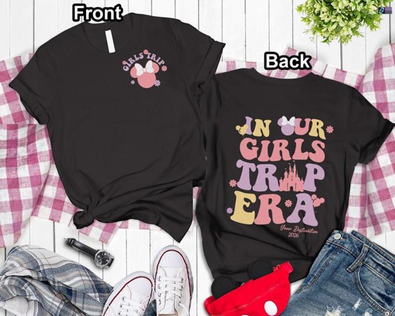 a pair of black t-shirts with a Disney-themed design, laid out on a white surface with a plaid cloth. The t-shirts have a front and back view, and the text "Girls Trip" and "In Our Girls" are visible on the front, along with the text "Your Reflection" and "Your Reflection 2020" on the back.