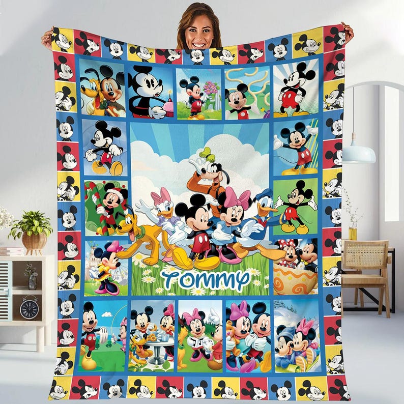 A woman is holding up a colorful quilt featuring various Disney characters, including Mickey Mouse, Minnie Mouse, Donald Duck, and Goofy.
