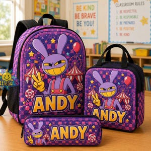 May include: A purple backpack, lunch bag, and pencil case set featuring a cartoon rabbit character making a peace sign. The items have a checkered pattern, carnival tent graphics, and the name ANDY printed in large yellow letters on each piece.