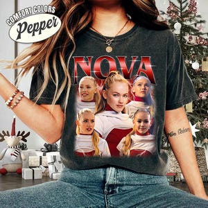 May include: Dark gray Comfort Colors Pepper t-shirt featuring the word "NOVA" in red and white, with a photo collage of five women. The shirt has a vintage look. The top left corner has the words "COMFORT COLORS" and "Pepper" in a white oval.