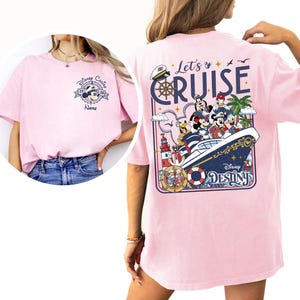 A woman wearing a pink t-shirt with a Disney Cruise-themed design, including Mickey Mouse and Minnie Mouse characters on a cruise ship.