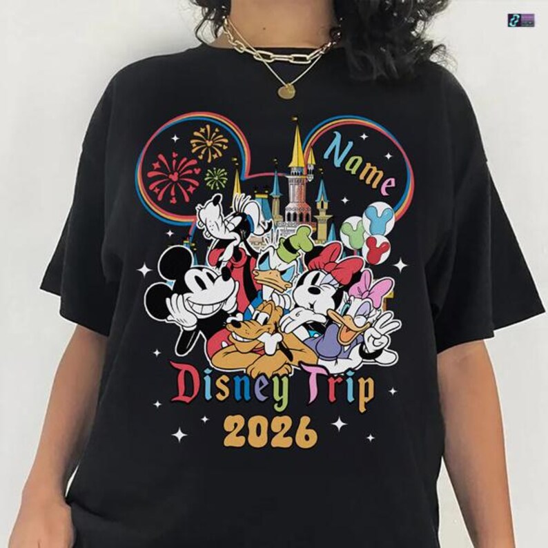 A person wearing a black t-shirt with a colorful graphic design featuring Disney characters and the text "Disney Trip 2026".