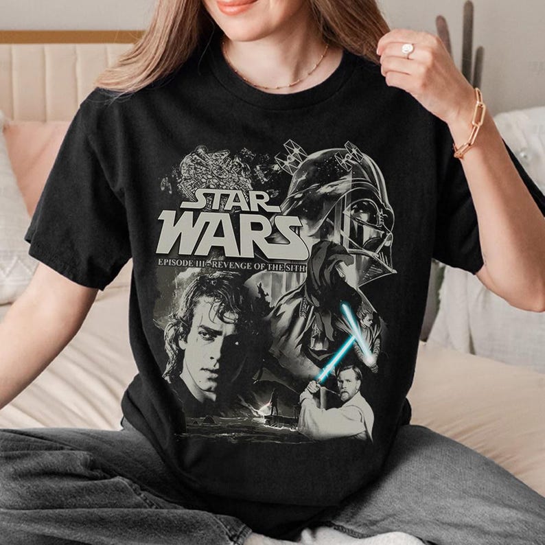 a woman sitting on a bed holding a star wars t - shirt