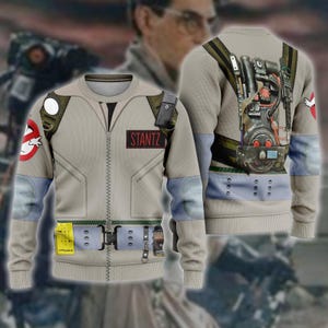 Puede incluir: Un suéter beige de manga larga y cuello redondo con un diseño estampado de uniforme de Ghostbusters. El frente muestra una etiqueta con el nombre STANTZ, mientras que la parte posterior presenta un gráfico detallado de un paquete de protones.