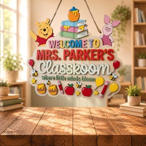 May include: A wooden classroom sign featuring Winnie the Pooh and Piglet, with text reading Welcome to Mrs. Parker's Classkoom where little minds bloom. The sign includes illustrations of honey pots, stacked books, apples, pencils, and bees.