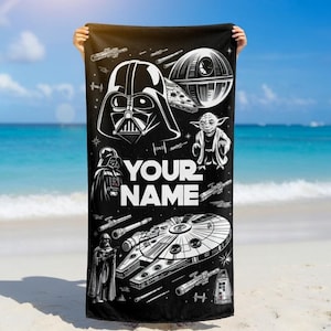 May include: Black beach towel featuring white illustrations of Star Wars characters, including Darth Vader, Yoda, and the Millennium Falcon. The towel has the text "YOUR NAME" in white. The towel is held up against a beach background.