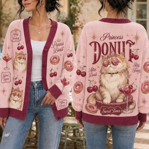 May include: A light pink button-down cardigan featuring a repeating pattern of cherries, donuts, and a cat wearing heart-shaped glasses. The back displays a large illustration of a cat with the text Princess DONUT and Sweet Times.