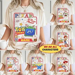 Puede incluir: Camisetas color crema con varios diseños de personajes de Toy Story. Cada camiseta tiene un gráfico central con el logotipo de Pixar, texto de Toy Story y un espacio para un nombre. Las camisetas también incluyen el texto "We do all characters."