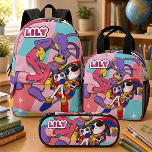 May include: A pink and blue backpack, lunch bag, and pencil case set featuring a cartoon character print and the name LILY in white letters. Each item displays a purple creature and a doll-like figure against a geometric background with stars.