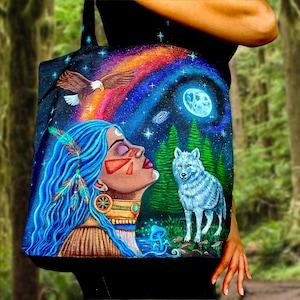 May include: A black tote bag featuring a vibrant, colorful illustration of a person with long blue hair adorned with feathers, a white wolf, a soaring eagle, a glowing moon, and a rainbow-colored nebula set against a dark forest background.