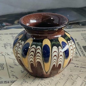 Può includere: Un piccolo vaso rotondo in ceramica marrone con un design astratto colorato. Il design presenta vortici di giallo, blu, verde e bianco.