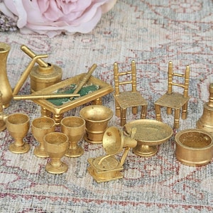 Puede incluir: Una colección de muebles y accesorios de casa de muñecas en miniatura de color dorado, que incluyen sillas, una mesa, copas, una jarra, un gramófono y una campana. Los artículos están dispuestos sobre una superficie estampada.