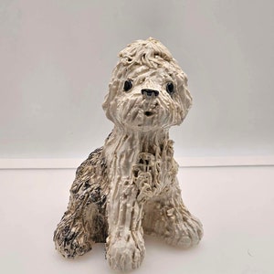 May include: A white ceramic dog figurine with black eyes and a black nose. The dog is sitting with its legs tucked under its body and its head tilted slightly to the side. The figurine is made in a textured style, giving the dog a fluffy appearance.