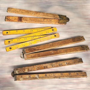 Puede incluir: Un conjunto de reglas plegables antiguas de madera y metal, con marcas de medición. Algunas son amarillas, otras marrones. Las reglas muestran medidas en centímetros.