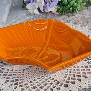 May include: Orange ceramic serving dish with a leaf-like design. The dish has a glossy finish and a sunburst pattern in the centre. The dish is divided into two sections, suitable for serving snacks or appetizers.