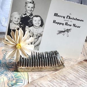 Op de afbeelding: Vintage kerstkaart met de boodschap "a Merry Christmas and a Happy New Year" en een zwart-wit foto van drie kinderen. Een crèmekleurige bloem en een bloemenkikker staan ook in de afbeelding. De items staan op een achtergrond van verouderd papier.