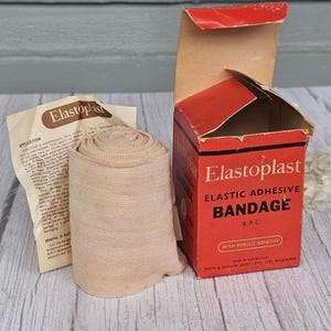Può includere: Una scatola rossa con il testo "Elastoplast Elastic Adhesive Bandage B.P.C. With Porous Adhesive" e un rotolo di bendaggio beige.