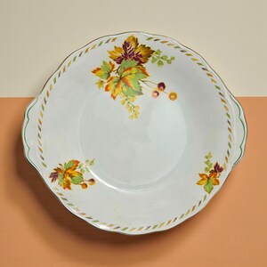 May include: White ceramic serving dish with a scalloped edge and two handles. The dish is decorated with colourful autumn leaves in shades of yellow, orange, and purple. A gold and green border frames the rim.