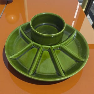 May include: A green ceramic serving dish with a central bowl and a divided outer section. The dish has a glossy finish and is designed for serving snacks or appetizers. The design is a mid-century modern style.