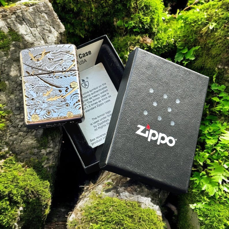 May include: A silver-tone Zippo Armor lighter featuring an intricate blue and gold dragon engraving, displayed in an open black presentation box with a white authentication card that includes the text Zippo and Armor case.