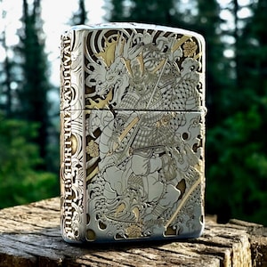 May include: A rectangular metal lighter featuring intricate silver and gold-toned engravings of a samurai and a dragon. The side of the lighter displays the text FORTES FORTUNA ADIUVAT in a vertical orientation, surrounded by detailed wave patterns.