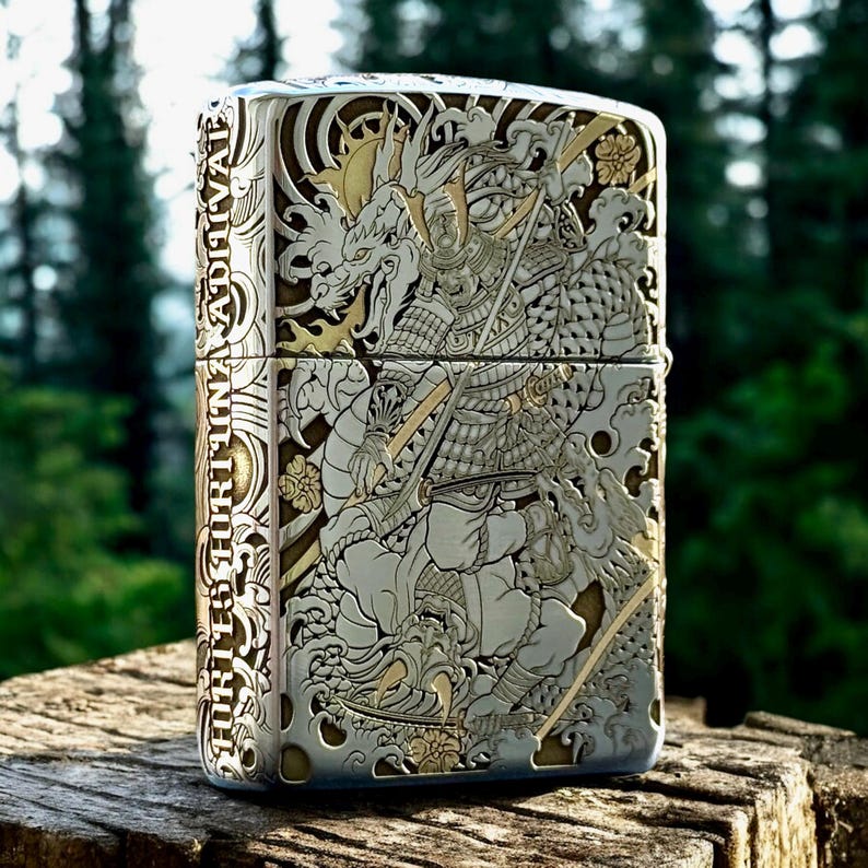 May include: A rectangular metal lighter featuring intricate silver and gold-toned engravings of a samurai and a dragon. The side of the lighter displays the text FORTES FORTUNA ADIUVAT in a vertical orientation, surrounded by detailed wave patterns.