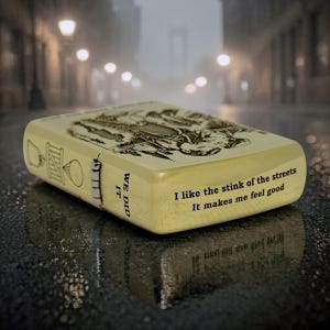 Pu&ograve; includere: Un accendino beige con un design inciso dettagliato e il testo "I like the stink of the streets. It makes me feel good." Il lato recita "WE DID IT". L'accendino &egrave; su una superficie bagnata.