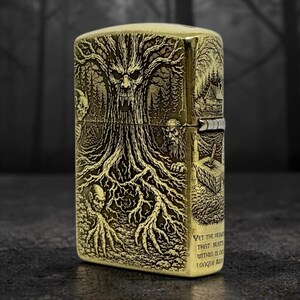 May include: A brass-colored lighter with an engraved forest scene featuring a tree with a face, figures, and a small house. The lighter has the text "Yet the heart that beats within is no longer alive."