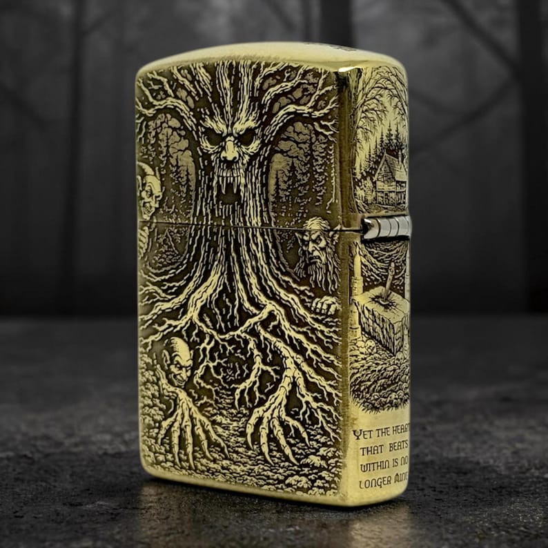 May include: A brass-colored lighter with an engraved forest scene featuring a tree with a face, figures, and a small house. The lighter has the text "Yet the heart that beats within is no longer alive."