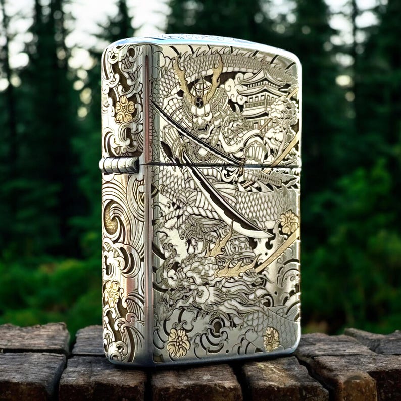 May include: A rectangular metal lighter with a polished silver finish featuring intricate laser-engraved details of a samurai warrior in armor, a large dragon, a traditional pagoda building, swirling wave patterns, and small floral accents.