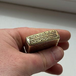 May include: A gold-colored metal lighter with engraved text: "I know of no better life purpose than to perish in attempting the great and the impossible." The lighter has a rectangular shape and a chain.