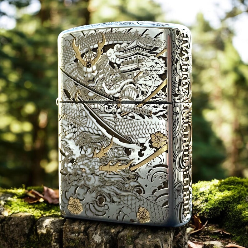 May include: A silver-toned metal lighter featuring an intricate engraved design of a samurai warrior holding a sword, a dragon, a pagoda, and floral motifs. The side of the lighter displays vertical text that reads INFINITY SURVIVAL.