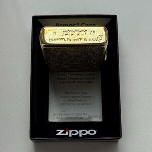 May include: A gold-colored Zippo lighter in its original black box. The lighter is engraved with a detailed pattern and the top is marked with "Zippo 25 BRADFORD, PA, MADE IN U.S.A." The box includes a card with information about the Armor case.