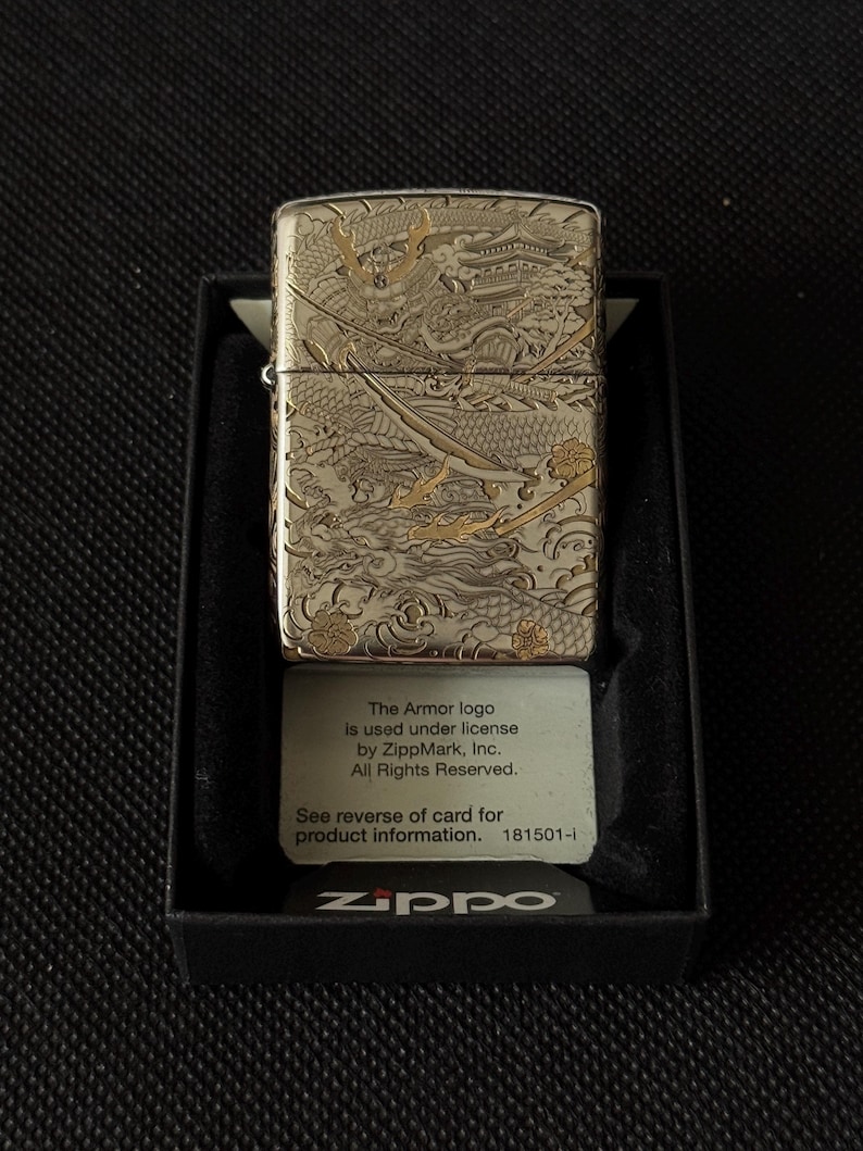 May include: A silver-tone metal lighter featuring an intricate engraved design of a samurai helmet, a sword, and a dragon. The lighter is housed in a black display box with a card that reads: The Armor logo Is used under license by ZippMark, Inc.