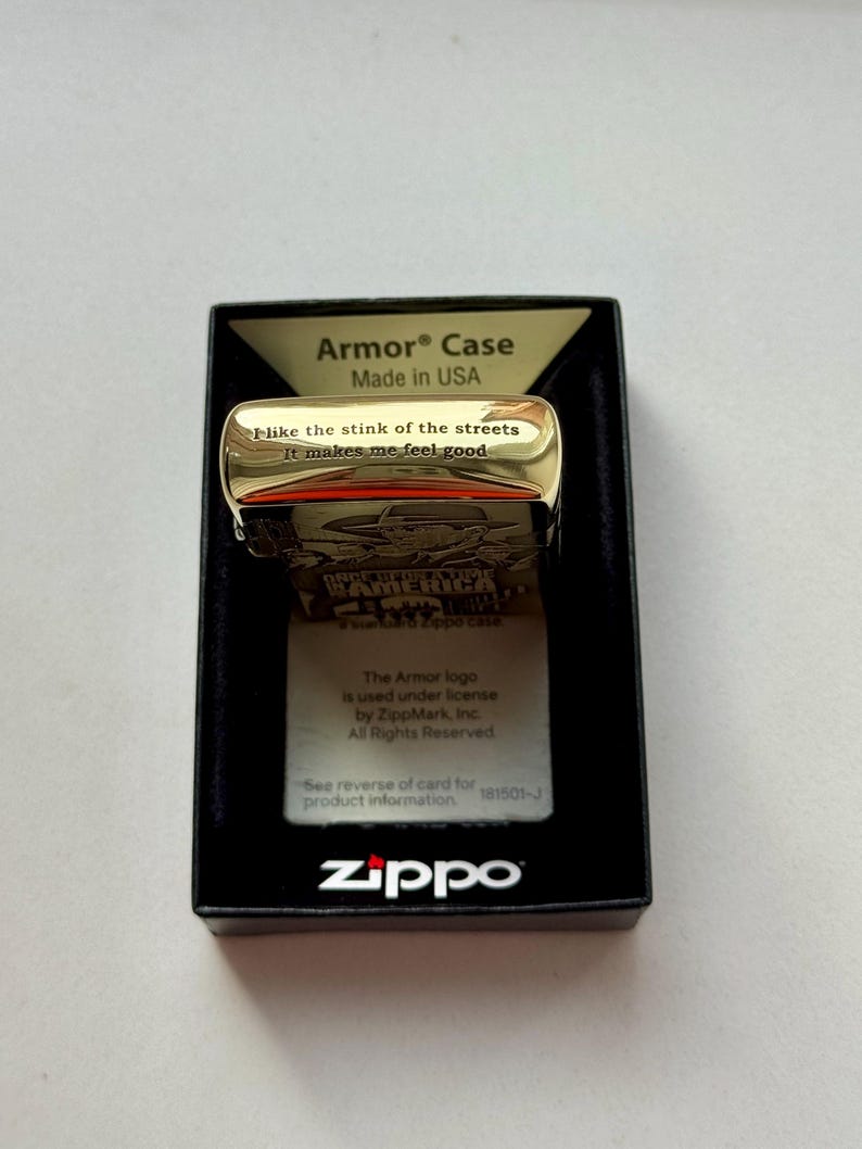 Pu&ograve; includere: Un accendino Zippo Armor Case color oro con la scritta "I like the stink of the streets, it makes me feel good". L'accendino &egrave; in una scatola nera con il logo Zippo e la scritta "Made in USA".