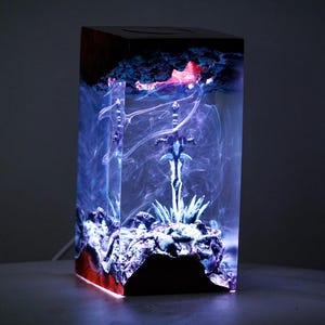 May include: A rectangular resin lamp with a sword design. The lamp features a blue and red color scheme with a glowing effect. The sword is positioned in the center, surrounded by a smoky, ethereal design.