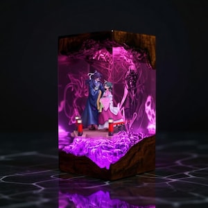 May include: A decorative resin block featuring a miniature scene with two figures in traditional Asian attire. The scene is illuminated with purple light, set within a wooden frame. The figures stand on a platform with red lanterns.