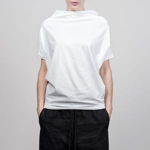 May include: A white, loose-fitting, short-sleeved shirt with a high neckline and black drawstring pants.