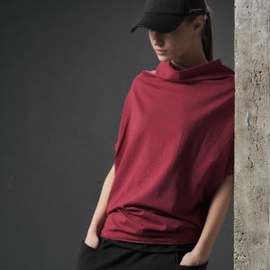 Może przedstawiać: Kobieta w luźnej, bordowej koszulce z krótkim rękawem i czapką z daszkiem w kolorze czarnym z napisem "Jaguars" z boku. Ma na sobie czarne spodnie z dużymi kieszeniami.