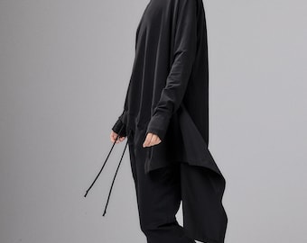 May include: A black long-sleeved tunic with an asymmetrical hemline and thin drawstrings, paired with matching black jogger-style pants and black leather ankle boots featuring side zippers. The outfit is monochromatic and features a loose fit.
