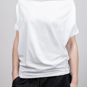 May include: A white, loose-fitting, short-sleeved t-shirt with a draped neckline. The shirt is made of a soft, comfortable fabric and has a relaxed fit.