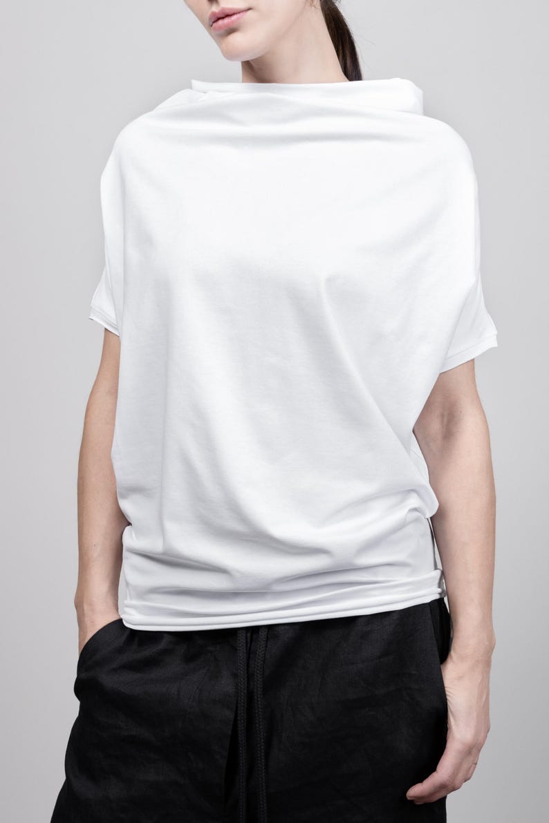 May include: A white, loose-fitting, short-sleeved t-shirt with a draped neckline. The shirt is made of a soft, comfortable fabric and has a relaxed fit.