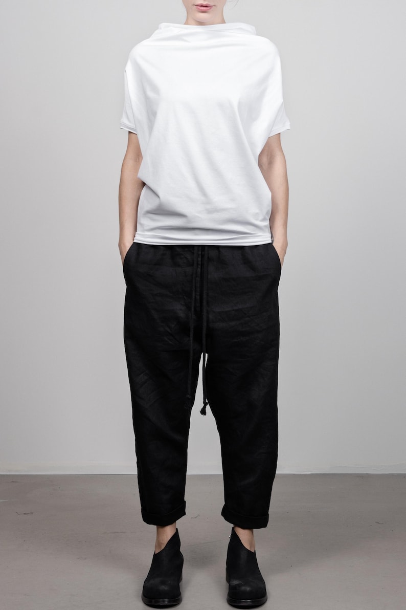 May include: A white, loose-fitting, short-sleeved shirt with a high neckline and black drawstring pants.