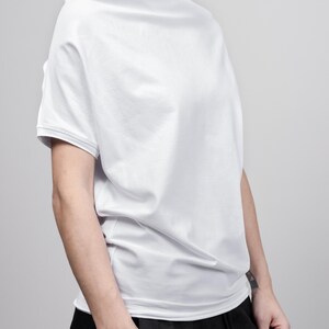 May include: A white, loose-fitting t-shirt with a slightly off-the-shoulder neckline. The shirt is made of a soft, comfortable fabric and has a relaxed fit.