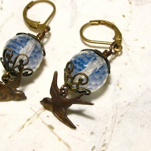 May include: A pair of earrings with a blue and white glass bead and a brass bird charm.