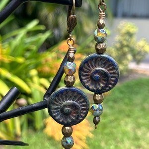 May include: A pair of dangle earrings with blue and gold ceramic beads and blue and green glass beads. The earrings have a brass hook closure.