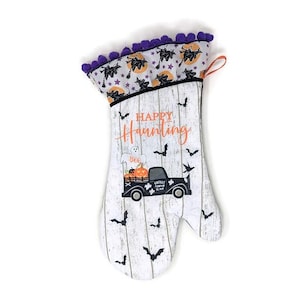 May include: White and black Halloween oven mitt with a "Happy Haunting" design. Features a black truck carrying pumpkins and a ghost. The top has a purple trim with black bats and orange stars.