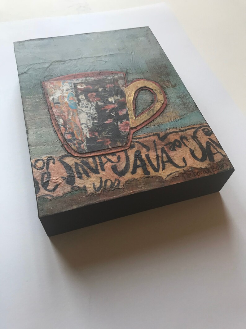 May include: A mixed media artwork featuring a brown and gold coffee cup with a textured background. The text "Java Java" is written in black paint on the bottom of the artwork. The artist's signature is visible in the bottom right corner.